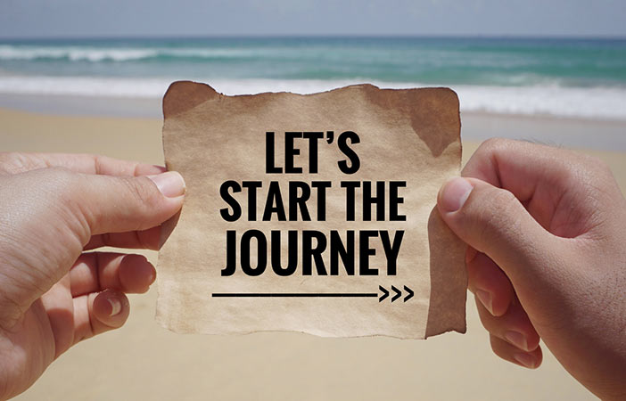 Hands holding a paper with the words 'Let's start the journey' written on it, against the backdrop of a tranquil beach scene. This image symbolizes the beginning of a transformative path towards anxiety relief through hypnotherapy.